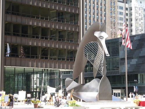 A large abstract metal sculpture of a horse-like figure in an urban plaza, surrounded by modern buildings.