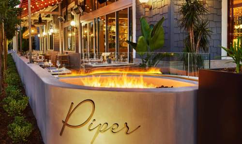 A modern outdoor dining area featuring a fire pit and the name "Piper" elegantly displayed on a curved wall.