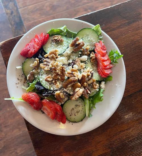 A fresh salad with mixed greens, cucumber slices, strawberries, walnuts, and a sprinkle of cheese on a white plate.