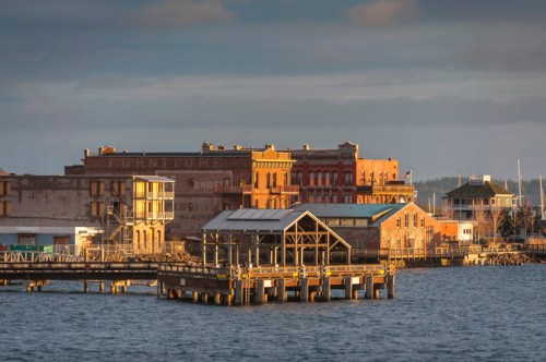 Historic waterfront buildings with a pier in the foreground, bathed in warm evening light.