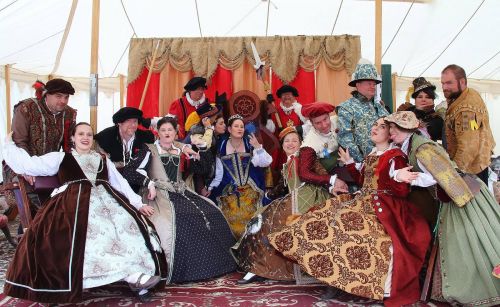 A group of people in elaborate historical costumes pose together in a tent, showcasing a festive atmosphere.