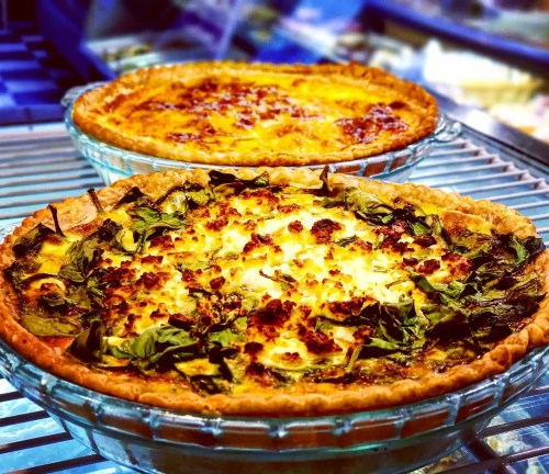 Two savory pies on a cooling rack, one with spinach and cheese, the other with a golden crust and melted cheese on top.