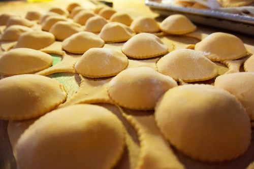 Close-up of uncooked ravioli on a wooden surface, showcasing their rounded shapes and dusted flour.