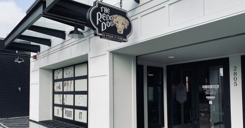 Exterior of The Redd Dog U-Pour It Pub, featuring a sign and large windows, with a modern building design.