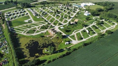 Aerial view of a campground with numerous RV sites, green fields, and a small pond surrounded by trees.
