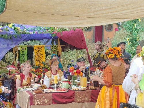A festive gathering with people in medieval costumes around a decorated table filled with food and drinks.
