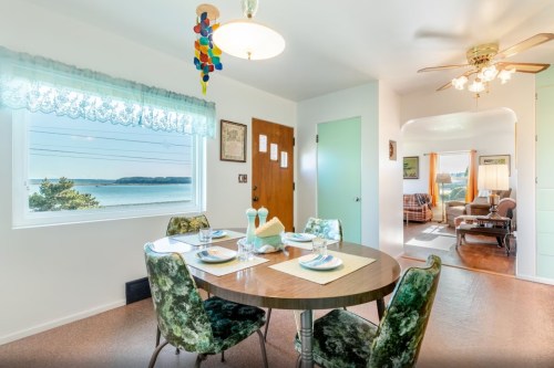 A cozy dining area with a round table set for four, overlooking a scenic view of water and a living room beyond.