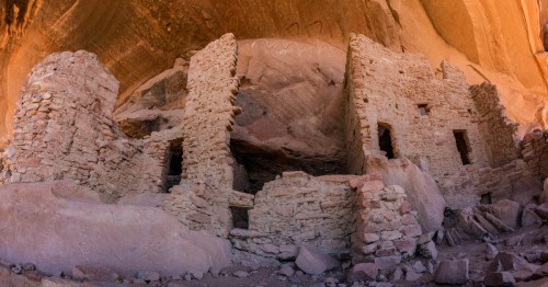 Ancient stone ruins nestled against a rocky cliff, showcasing weathered walls and openings in a desert landscape.