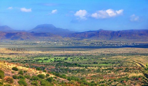 A panoramic view of a valley with mountains in the background, featuring green fields and a clear blue sky.