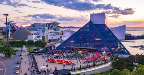 Aerial view of a lively outdoor event at the Rock and Roll Hall of Fame, with a sunset over the waterfront.