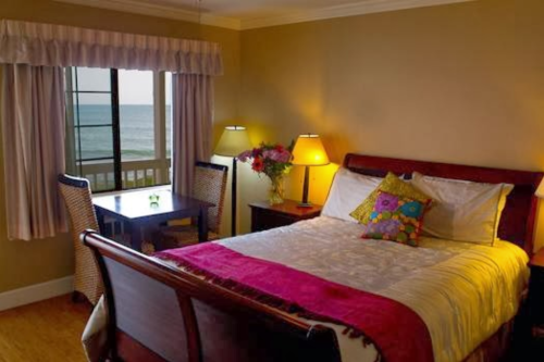 Cozy bedroom with a large bed, colorful pillows, lamps, and a view of the ocean through a window.