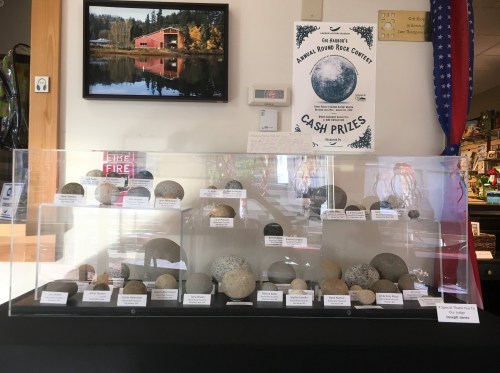 Display case with various rocks labeled, a poster for a rock contest, and a scenic photo of a lake in the background.