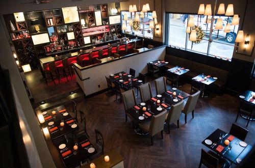 A modern restaurant interior featuring tables, chairs, and a bar area with warm lighting and a cozy atmosphere.