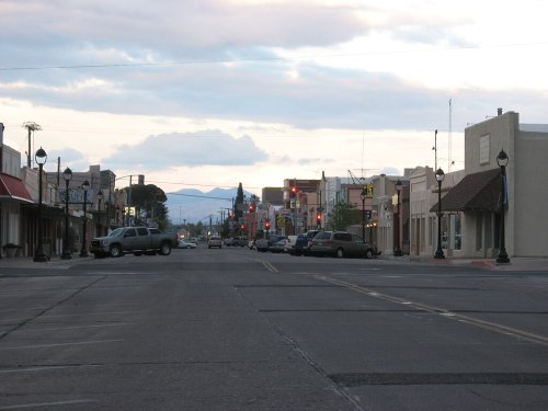 A quiet street in a small town at dusk, with buildings lining the road and mountains in the background.