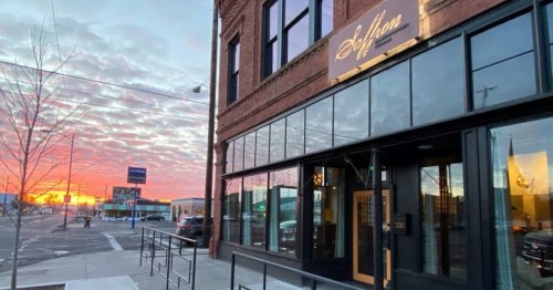 Exterior of a restaurant at sunset, featuring large windows and a sign that reads "Soflora." Colorful clouds in the sky.