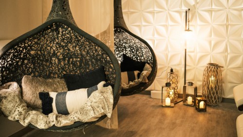 Two stylish hanging chairs with cushions, surrounded by decorative lanterns and a textured wall, creating a cozy atmosphere.