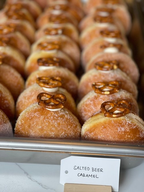 A tray of sugar-coated donuts topped with pretzels, labeled "Salted Beer Caramel."