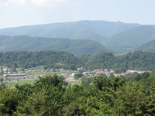 A scenic view of a small town surrounded by lush green mountains under a clear blue sky.
