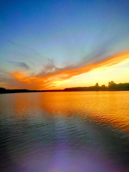 A serene lake at sunset, with vibrant orange and blue skies reflecting on the calm water.