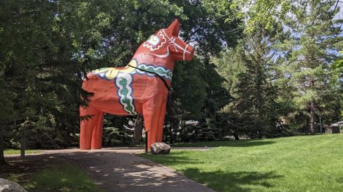 A large, colorful Dala horse statue stands in a park surrounded by trees and green grass.