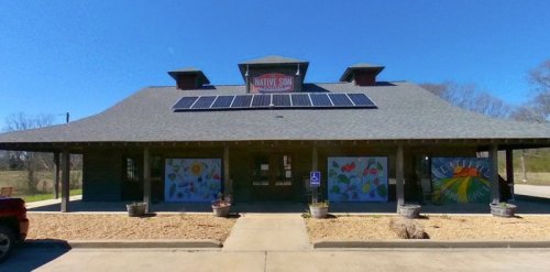 A large building with a gray roof, solar panels, and colorful murals on the sides, set against a clear blue sky.