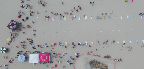 Aerial view of a beach with people, colorful umbrellas, and beach towels arranged in lines on the sand.