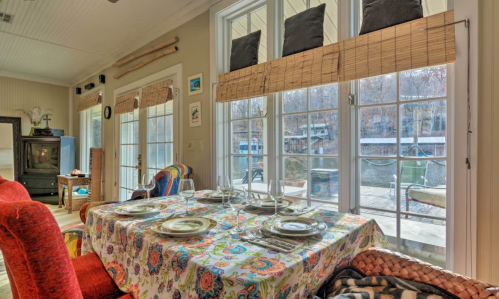 A cozy dining area with a colorful tablecloth, set for a meal, and large windows overlooking a scenic outdoor view.