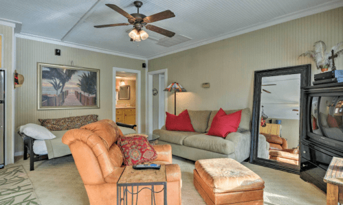 Cozy living room with a ceiling fan, two sofas, a coffee table, and a large mirror, featuring warm colors and decor.