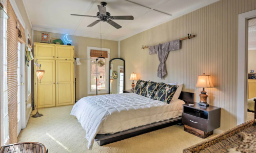 Cozy bedroom with a queen bed, yellow wardrobe, and natural light from large windows. Warm, inviting decor.