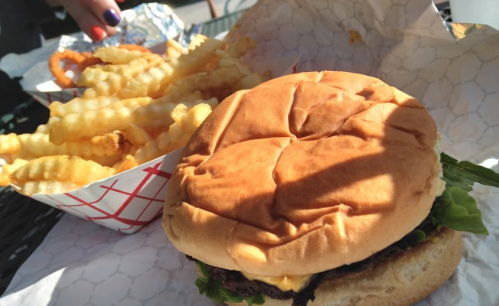 A close-up of a burger with lettuce and cheese next to a serving of crinkle-cut fries in a red and white container.