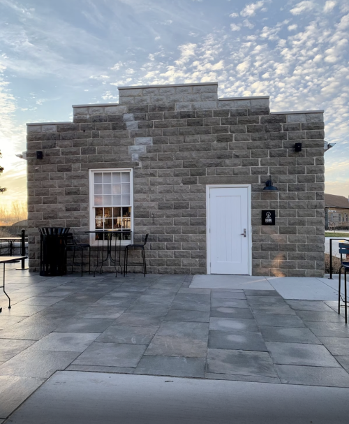 A stone building with a white door and window, surrounded by a paved area and outdoor seating.