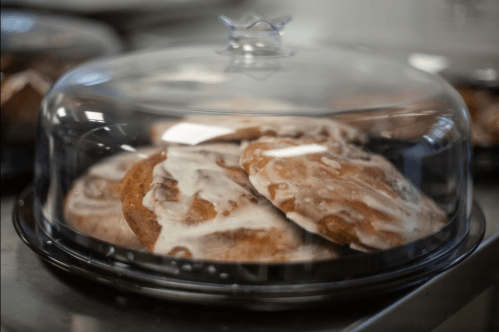 A glass cloche covers a plate of frosted cookies, showcasing their soft texture and sweet glaze.