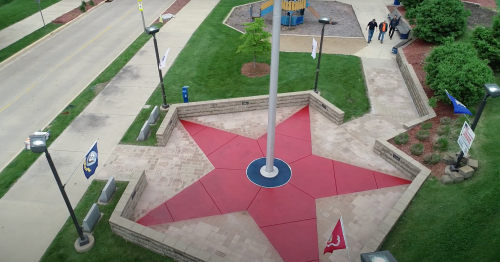 Aerial view of a red star-shaped plaza with a flagpole, surrounded by green grass and pathways.