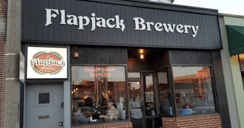 Exterior of Flapjack Brewery with a sign, large windows, and patrons inside. The atmosphere is warm and inviting.