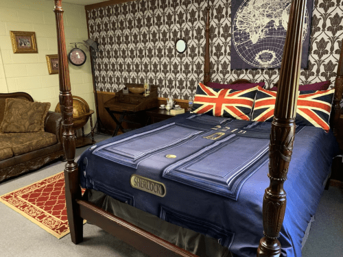 A cozy bedroom featuring a four-poster bed with a Sherlock-themed duvet, Union Jack pillows, and vintage decor.