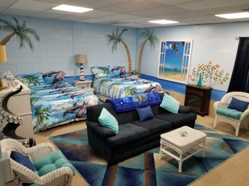 A cozy beach-themed room with two beds, a sofa, and tropical decor, featuring palm trees and ocean views.