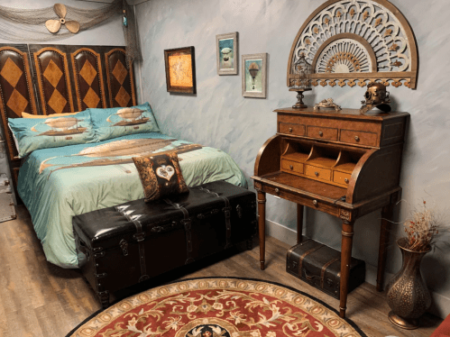 Cozy bedroom with a bed, decorative pillows, vintage desk, and a patterned rug, featuring warm, inviting colors.