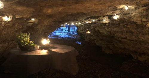 A cozy cave interior with string lights, a lantern, and a table with plants, creating a warm atmosphere.