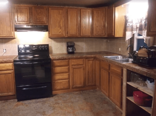 A cozy kitchen with wooden cabinets, a black stove, and a sink, featuring a tiled backsplash and countertop.