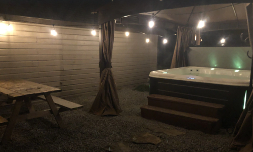 A cozy outdoor space featuring a hot tub, picnic table, and string lights under a canopy.