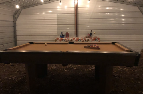 A dimly lit indoor space featuring a pool table with a rack of balls and a decorative table in the background.