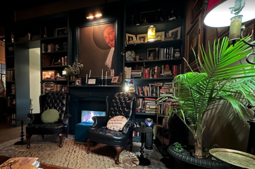 Cozy living room with two armchairs, a fireplace, bookshelves, and a large portrait on the wall. A plant adds greenery.