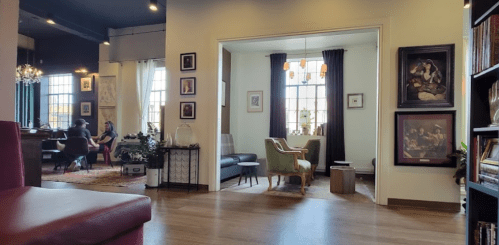 A cozy interior with two rooms; one features a piano, the other has a dining area with art on the walls.
