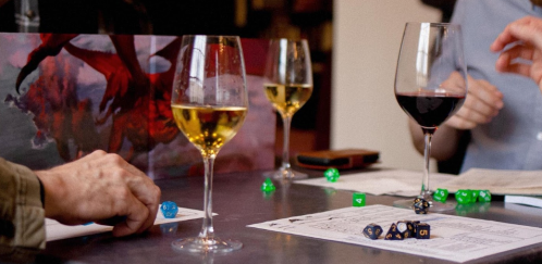 A tabletop gaming scene with dice, character sheets, and glasses of wine on a table.