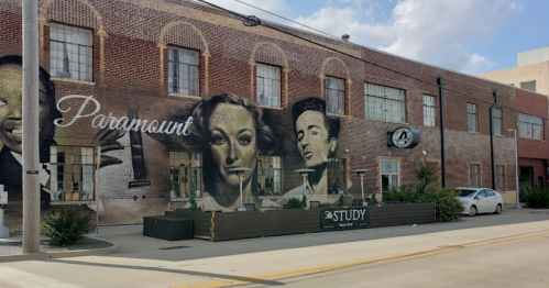 Mural on a brick building featuring black-and-white portraits, with a sign for "The Study" in front.
