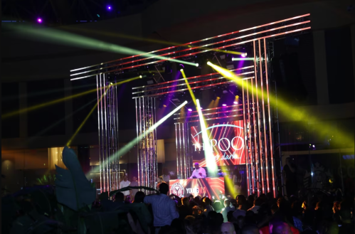 A lively concert scene with a DJ on stage, colorful lights, and a crowd enjoying the music.