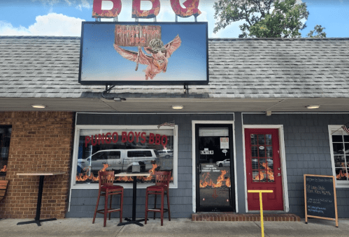 Exterior of Pungo Boys BBQ with a sign featuring a winged pig and outdoor seating.