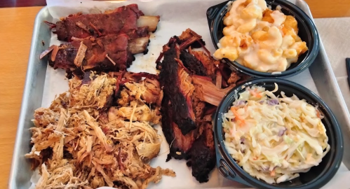 A tray of barbecue featuring pulled pork, beef brisket, macaroni and cheese, and coleslaw.