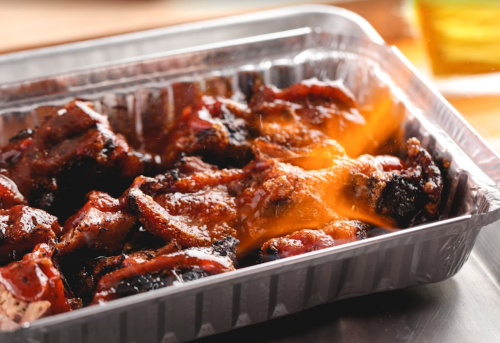 A tray of grilled meat coated in barbecue sauce, with some pieces charred and sizzling.