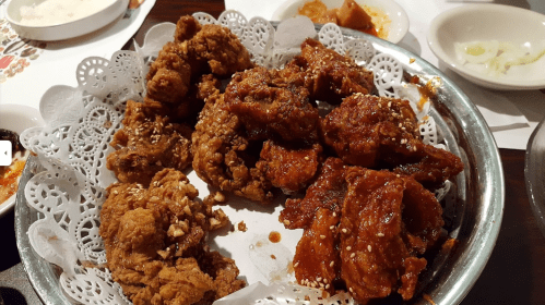 A platter of crispy fried chicken pieces, some coated in sesame seeds, served with side dishes.